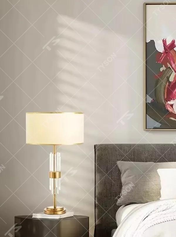 Light luxury style crystal and metal segmented table lamp, featuring transparent crystal columns paired with gold metal accessories, and an off-white fabric lampshade with a gold trim at the bottom. It emits soft and warm light, combining decorativeness and practicality, suitable for lighting and decoration in spaces such as bedroom nightstands, living room side tables, and hotel guest rooms.