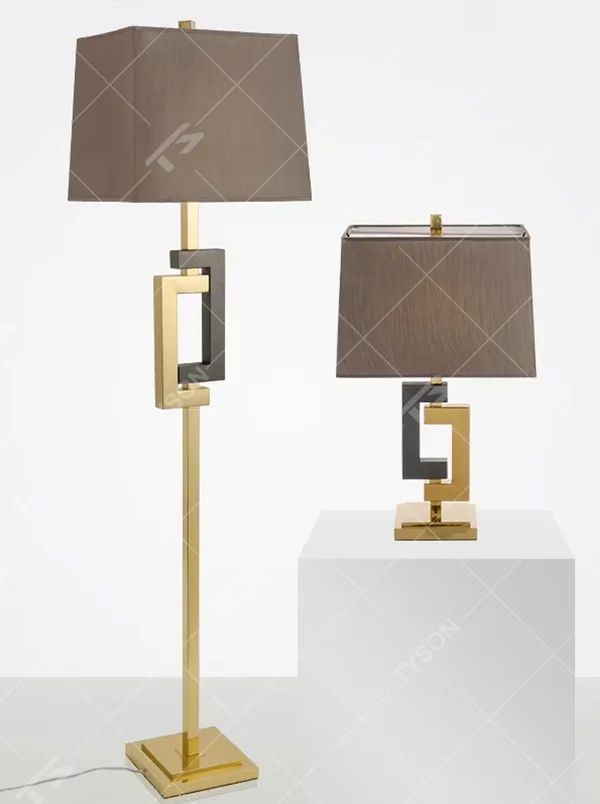 This is a modern light luxury geometric interlocking table lamp, featuring an interlocking geometric lamp body crafted from gold and gray dual-color metal, paired with a dark gray fabric lampshade. It emits soft and uniform light, serving both lighting and decorative purposes, suitable for bedroom nightstands, light luxury living room side tables, hotel guest rooms, showrooms and other scenarios.