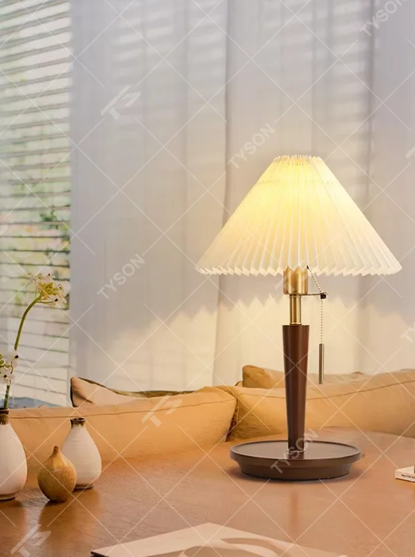 Vintage Nordic pleated fabric table lamp, with an off-white pleated fabric lampshade paired with a dark brown wood and gold metal spliced lamp pole, featuring a pull-cord switch, emitting soft and warm light, combining decorativeness and practicality, suitable for lighting and decoration in spaces such as bedroom nightstands, living room side tables, and B&B guest rooms.