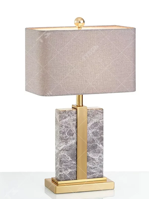 Modern light luxury marble and metal spliced table lamp, with a gray marble lamp body paired with gold metal decorative strips, a light gray fabric rectangular lampshade (with a gold ball decoration on top), emitting soft and elegant light, combining decorativeness and practicality, suitable for lighting and decoration in spaces such as bedroom nightstands, living room side tables, and hotel guest rooms.