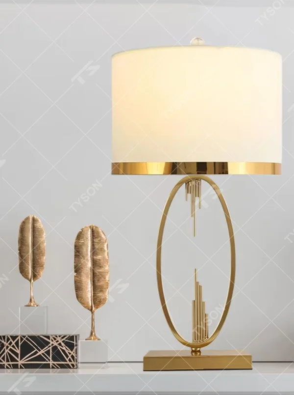 Light luxury style gold metal table lamp, featuring an oval hollow frame with pendant line decorations, paired with an off-white fabric lampshade with a gold trim at the bottom. It emits soft and elegant light, combining artistic decorativeness and lighting practicality, suitable for atmosphere creation and embellishment in bedrooms, living rooms, hotels and other spaces.