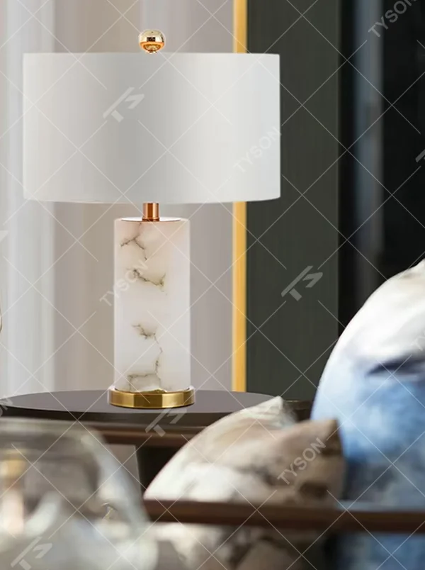 This is a light luxury minimalist table lamp, featuring a natural marble lamp post paired with gold metal accents and an off-white fabric lampshade. It emits soft and gentle light, serving both lighting and decorative purposes, suitable for bedroom nightstands, hotel guest rooms, light luxury living room side tables, showrooms and other scenarios.