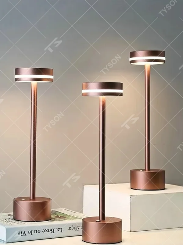Modern minimalist bronze metal rechargeable table lamp, featuring a cylindrical lamp body and a top ring-shaped lighting design, emitting soft and even light. It supports wireless battery life and touch dimming, suitable for ambient lighting and supplementary lighting in scenarios such as dining tables, bars, and bedroom nightstands.