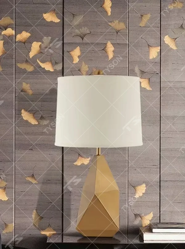 Modern light luxury style geometric cut metal table lamp, featuring a gold rhombus lamp body paired with an off-white fabric lampshade (with a gold trim at the bottom), designed for both tabletop placement and hanging. It emits soft and warm light, combining decorativeness and practicality, suitable for lighting and decoration in spaces such as living room side tables, bedroom nightstands, and hotel guest rooms.