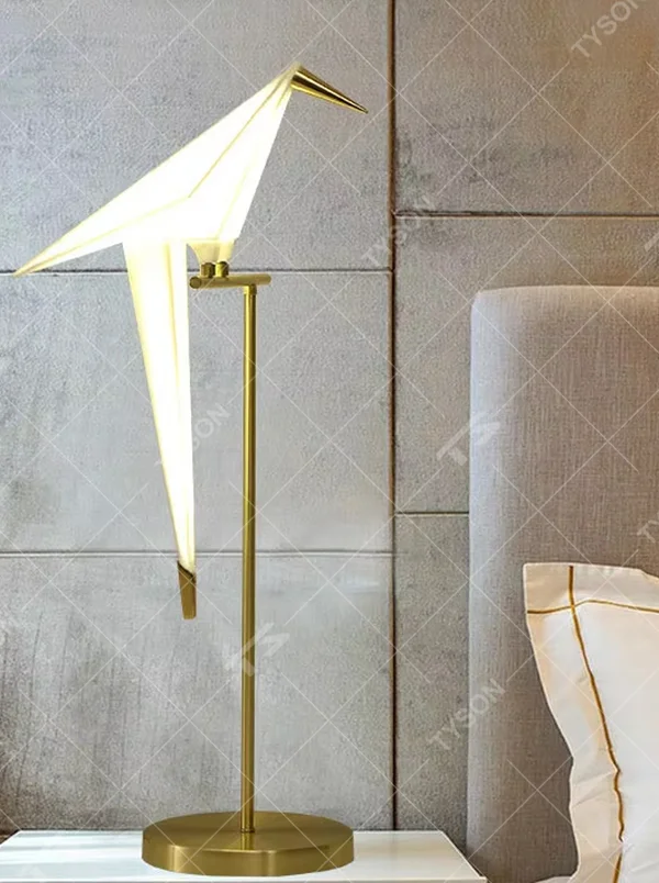 This is a modern light luxury origami crane-shaped table lamp, featuring a gold metal stand paired with a translucent paper art lamp body. The lamp body is as dynamic and soft as an origami crane, serving both lighting and artistic decoration purposes, suitable for bedroom nightstands, light luxury living room side tables, hotel guest rooms, showrooms and other scenarios.
