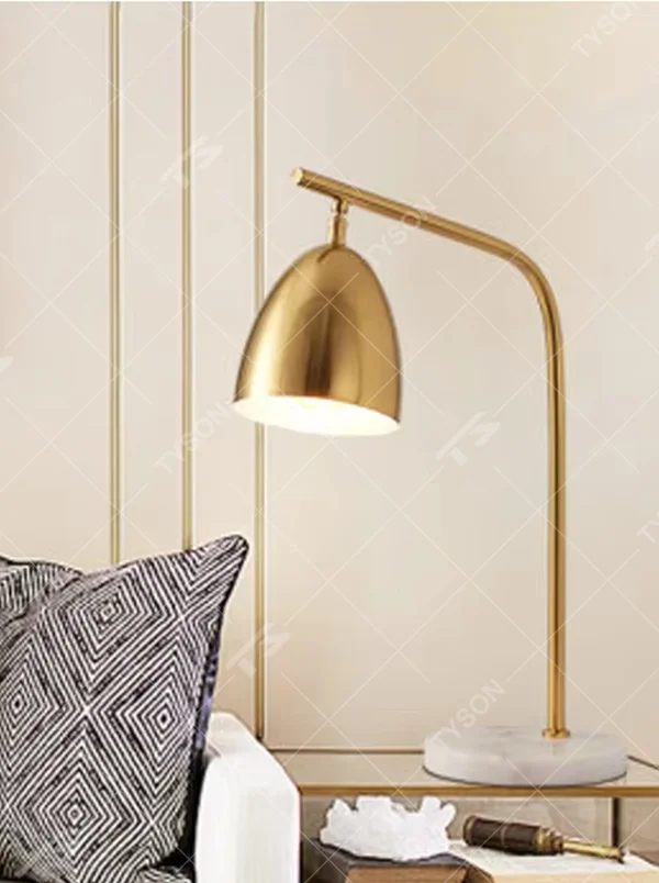 This is a modern light luxury style table lamp, with a gold metal curved arm paired with a dome-shaped lampshade, and a white marble base, which has both lighting and decorative functions, suitable for study desks, bedroom nightstands, office spaces, etc.