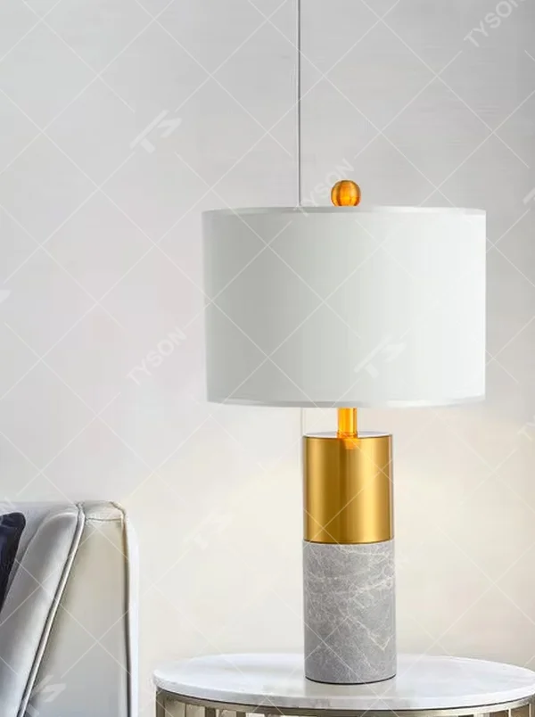 This is a light luxury marble-metal splicing table lamp, with a white fabric lampshade paired with a base made of gold metal and gray marble, accented with an orange decorative ball on top, featuring both decorative and lighting functions, ideal for high-end indoor scenarios such as bedroom nightstands and living room side tables.
