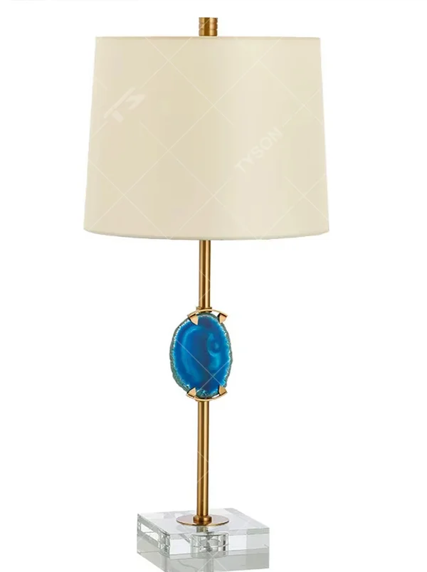 This is a light luxury agate decorative table lamp, with an off-white fabric lampshade paired with a gold metal lamp pole, inlaid with a natural blue agate slice in the middle, and a transparent crystal square base, featuring both decorative and lighting functions, ideal for high-end indoor scenarios such as bedroom nightstands and living room side tables.