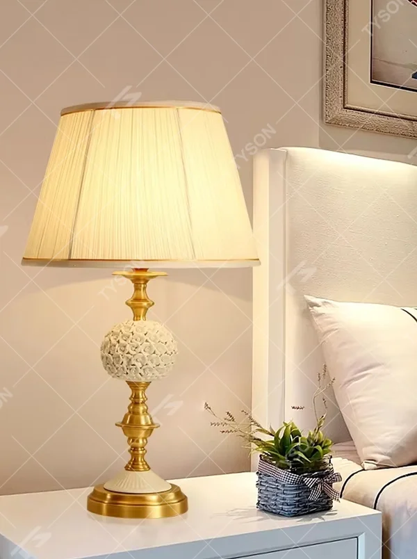 This European light luxury table lamp features a glossy gold metal base, paired with hollow carved crystal decorations and an off-white pleated fabric lampshade, presenting a luxurious and retro court texture. The light is soft and warm, serving both lighting and decorative purposes, suitable for placement in European-style spaces such as bedrooms and villa guest rooms.