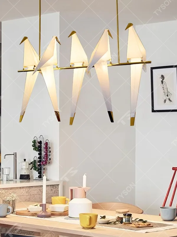 A modern art style linear chandelier in the shape of origami cranes, featuring a gold metal frame paired with translucent paper origami crane lampshades. It emits a soft and warm glow when lit, combining artistic decoration with lighting functionality, ideal for creating a soothing and romantic space atmosphere.
