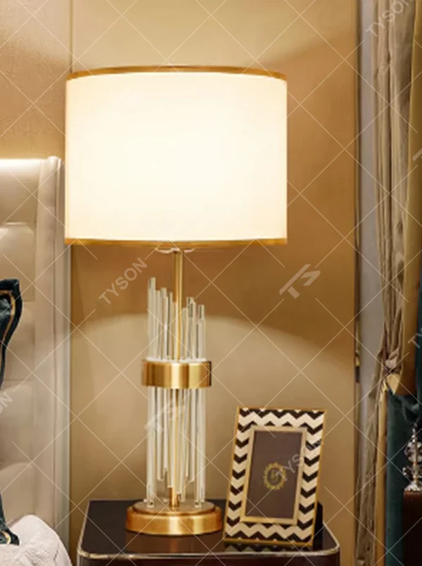 This is a light luxury crystal-metal splicing table lamp, with an off-white fabric lampshade edged with gold trim, a lamp post made of transparent crystal strips and gold metal, and a gold metal base, featuring both decorative and lighting functions, ideal for high-end indoor scenarios such as bedroom nightstands and living room side tables.