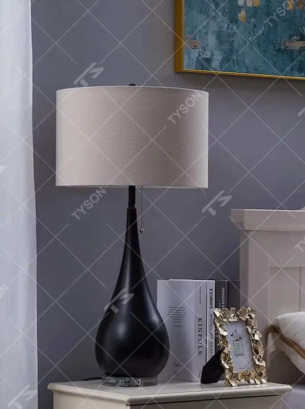 This is a pastoral-style floral fabric table lamp, with an off-white lampshade printed with blue and black floral patterns, paired with a black matte teardrop-shaped base and transparent crystal feet, featuring both decorative and lighting functions, ideal for warm indoor scenarios such as bedroom nightstands and living room side tables.