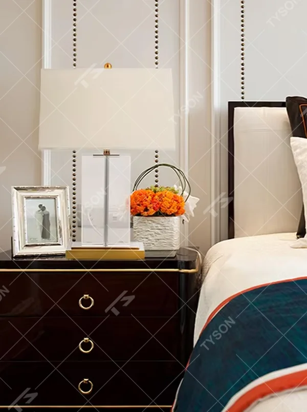 This modern light luxury table lamp features an off-white fabric lampshade (trimmed with a thin gold edge), paired with a transparent crystal square column lamp pole and a gold metal base. The overall style is simple and elegant, with soft eye-protective light, serving both lighting and decorative purposes, suitable for modern light luxury style spaces such as bedrooms, living rooms, and hotel guest rooms.