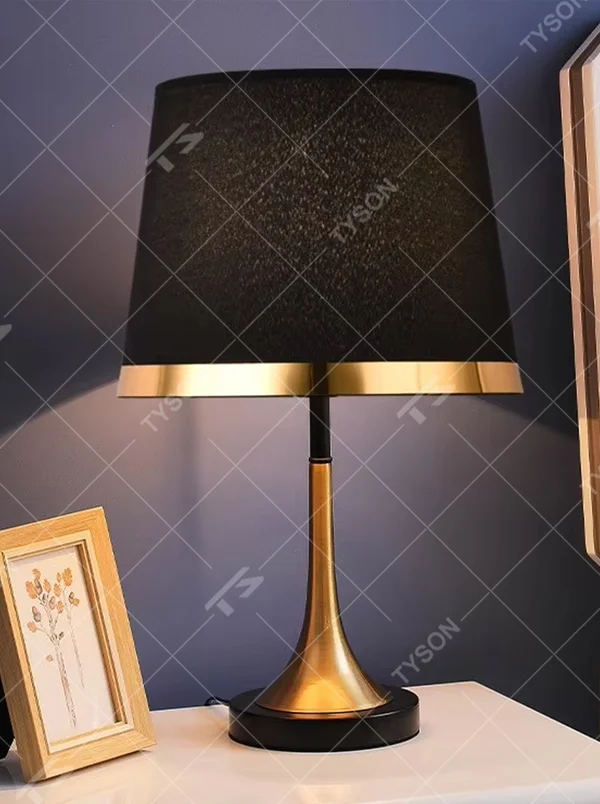 This modern light luxury table lamp features a black fabric cylindrical lampshade, paired with a black and gold contrasting metal lamp pole. The lower part is a trumpet-shaped gold metal design, and the base is black. The overall style is simple and elegant, with soft, non-glaring light, serving both lighting and decorative purposes, suitable for bedrooms, studies, living rooms and other spaces.
