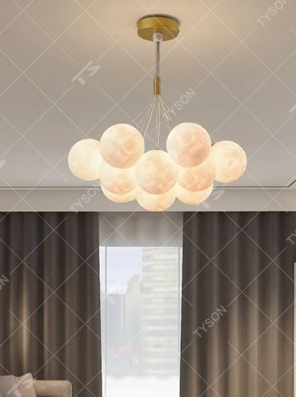 A modern light luxury style moon cluster chandelier, featuring a gold metal frame paired with multiple moon-textured glowing spheres and one colorful nebula sphere. It emits a soft and dreamy glow when lit, combining decorative appeal with practical illumination, ideal for creating a romantic and playful space atmosphere.
