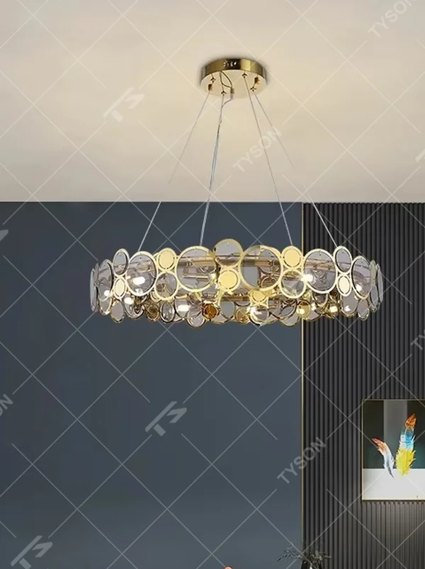 A modern light luxury style linear chandelier, featuring a gold metal frame with interlocked circular transparent glass panels and gold rings. It emits a brilliant yet soft glow when lit, combining decorative appeal with practical illumination, ideal for creating a sophisticated and high-end space atmosphere.