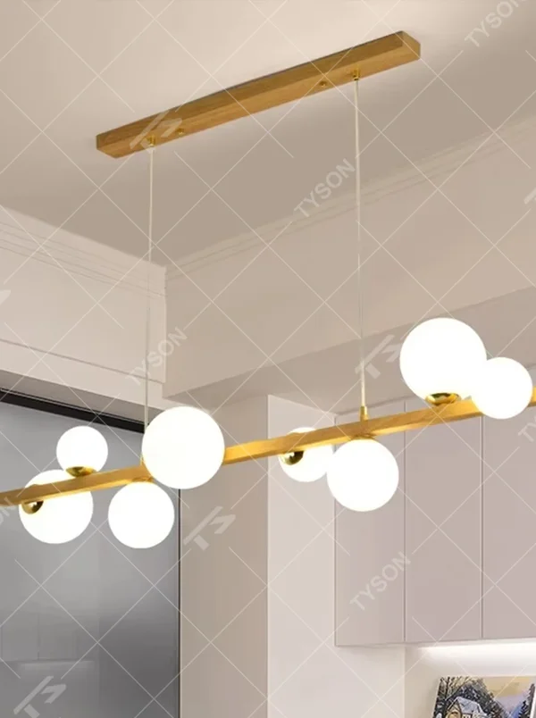 Nordic-style gold linear chandelier with a wood-like finish, paired with multiple round milk-white glass ball lampshades. It features a simple and lightweight design, emitting soft and gentle light, serving as a modern home lighting fixture that combines illumination and decoration.
