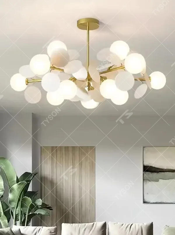 Modern light luxury firefly chandelier, featuring a radial branch frame in brass metal paired with clustered milk-white frosted glass balls to form a starburst shape. It emits soft and translucent light, combining a dreamy feel and elegant ambiance, making it a high-end decorative lighting fixture that elevates the space's style.