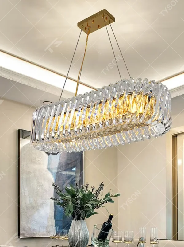 This modern light luxury linear crystal chandelier features a gold metal ceiling base, enclosed by wavy transparent crystal strips to form a full linear shape. When lit, light refracts through the crystal to emit a brilliant and soft glow, combining a transparent texture with an ambient atmosphere. Ideal for dining rooms, bars, light luxury apartments, and other spaces, it adds an exquisite and sophisticated touch to modern minimalist or light luxury home environments.