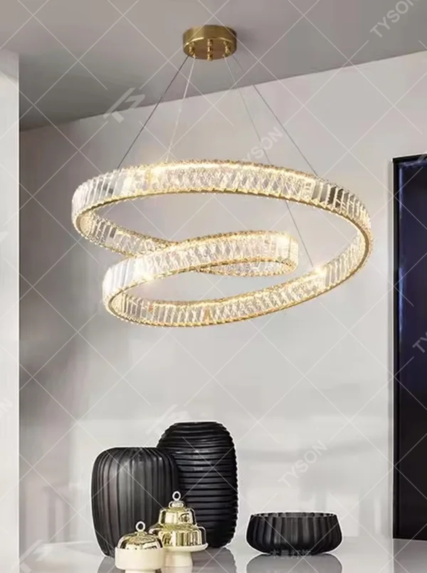 This modern light luxury interwoven ring crystal chandelier features a gold metal frame, inlaid with transparent long crystals to create a dynamic interwoven double-ring shape. When lit, light refracts through the crystal to emit a brilliant and soft glow, combining a futuristic feel with an ambient atmosphere. Ideal for dining rooms, living rooms, light luxury apartments, and other spaces, it adds an exquisite and sophisticated touch to modern minimalist or light luxury home environments.