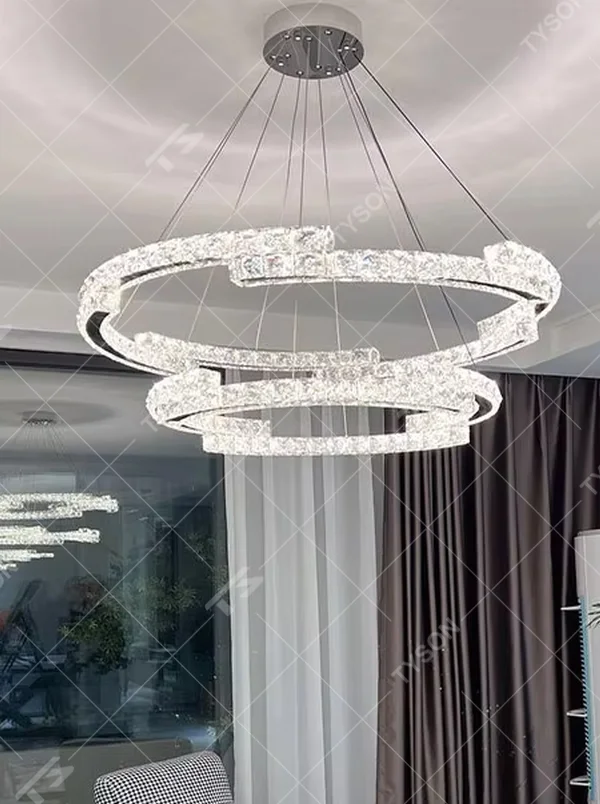 This modern light luxury double-ring interwoven crystal chandelier features a silver metal base, inlaid with transparent crystals to create a dynamic double-ring interwoven shape. When lit, light refracts through the crystal to emit a brilliant and dynamic glow, combining a futuristic feel with an ambient atmosphere. Ideal for living rooms, dining rooms, light luxury apartments, and other spaces, it adds an exquisite and sophisticated touch to modern minimalist or light luxury home environments.
