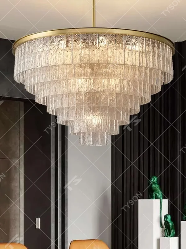 This modern light luxury layered conical chandelier features a gold metal top frame, with multiple layers of textured glass strips hanging down to form a conical layered shape. When lit, light refracts through the glass to emit a brilliant and soft glow, combining a luxurious texture with an ambient atmosphere. Ideal for high-ceiling living rooms, villas, light luxury apartments, and other spaces, it adds an exquisite and sophisticated touch to modern minimalist or light luxury home environments.
