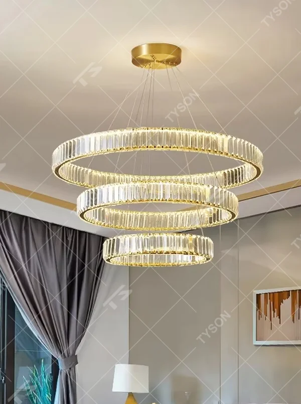 This modern light luxury multi-ring crystal chandelier consists of multiple crystal rings of varying sizes suspended in a staggered layout, each inlaid with transparent long crystals and adjustable via gold suspension wires. When lit, light refracts through the crystal to emit a brilliant and soft glow, combining layered design with an ambient atmosphere. Ideal for high-ceiling living rooms, villa foyers, hotel lobbies, or duplex spaces, it adds an exquisite and sophisticated touch to modern light luxury or minimalist environments.