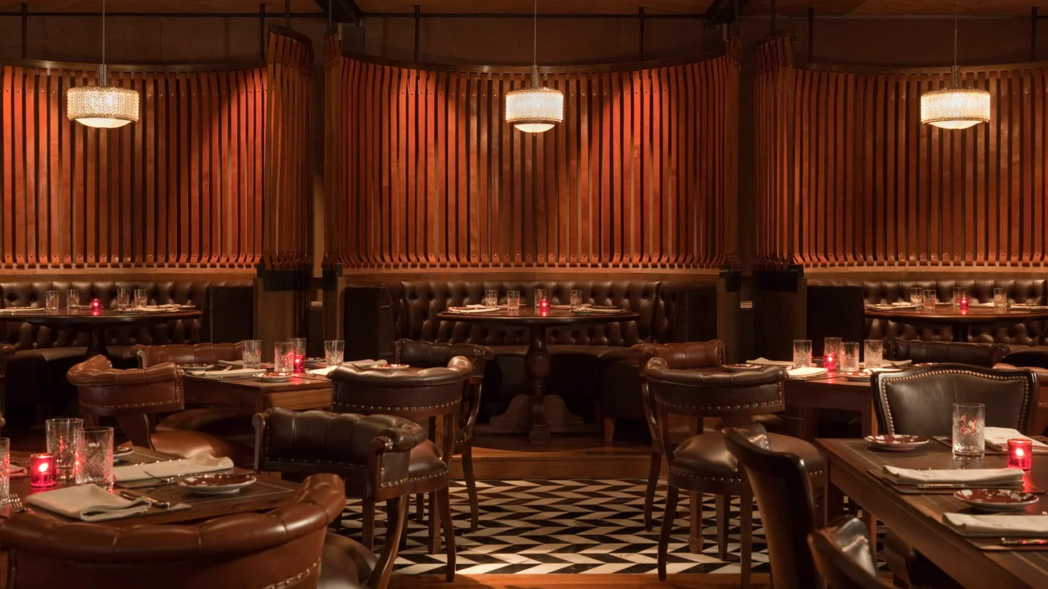Sophisticated restaurant interior with warm crystal pendant lights, tufted leather booths, and rich wooden paneling, showcasing luxurious ambient Lighting Trends for upscale dining spaces