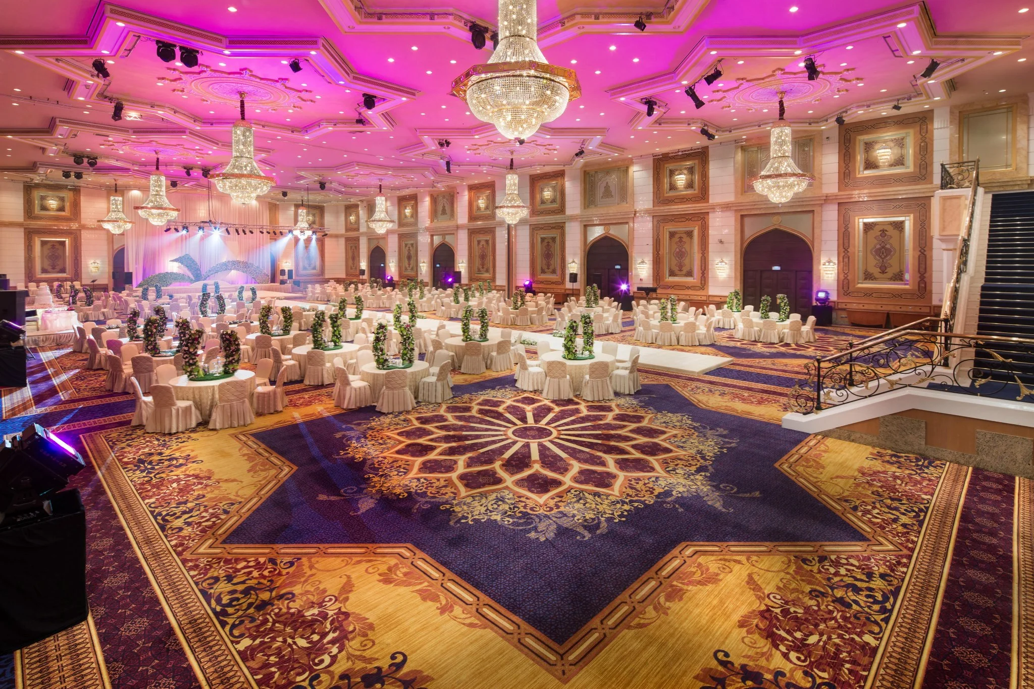 Opulent grand ballroom with ornate crystal chandeliers, vibrant pink ambient lighting, and intricate decor, illustrating Lighting Balance Beauty and Cost in luxury event venue design