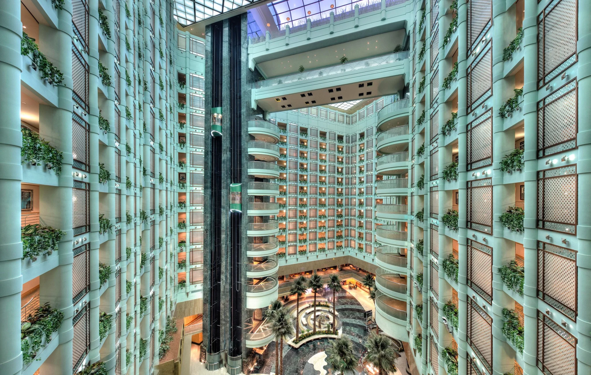 Grand atrium hotel corridor with multi-story balconies, glass ceiling, and ambient lighting fixtures, highlighting sophisticated Hotel Corridor Lighting in a luxury tropical resort setting